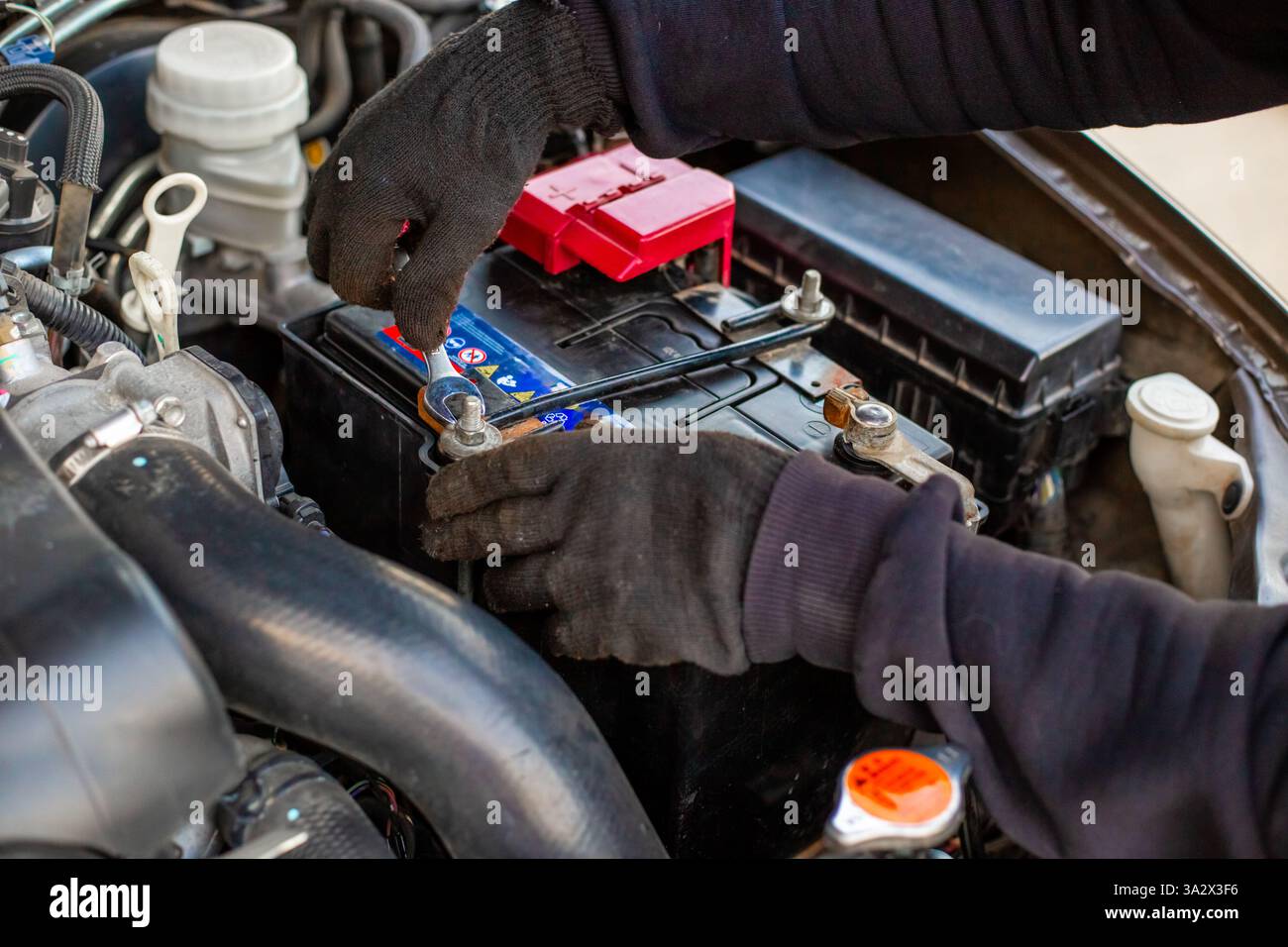 Remplacement de la batterie d'une voiture. Le mécanicien installe la batterie en fixant le support de montage de la batterie avec une clé. Banque D'Images