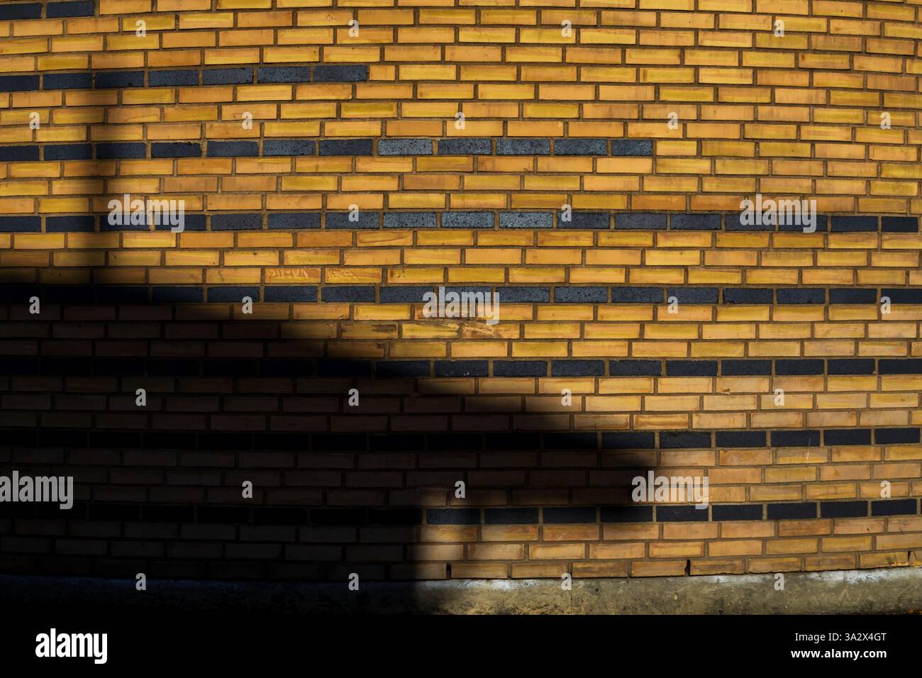 Un mur de briques jaunes avec plusieurs lignes de briques noires est transformé par une ombre, créant une illusion abstraite ressemblant à un vaisseau amarré Banque D'Images