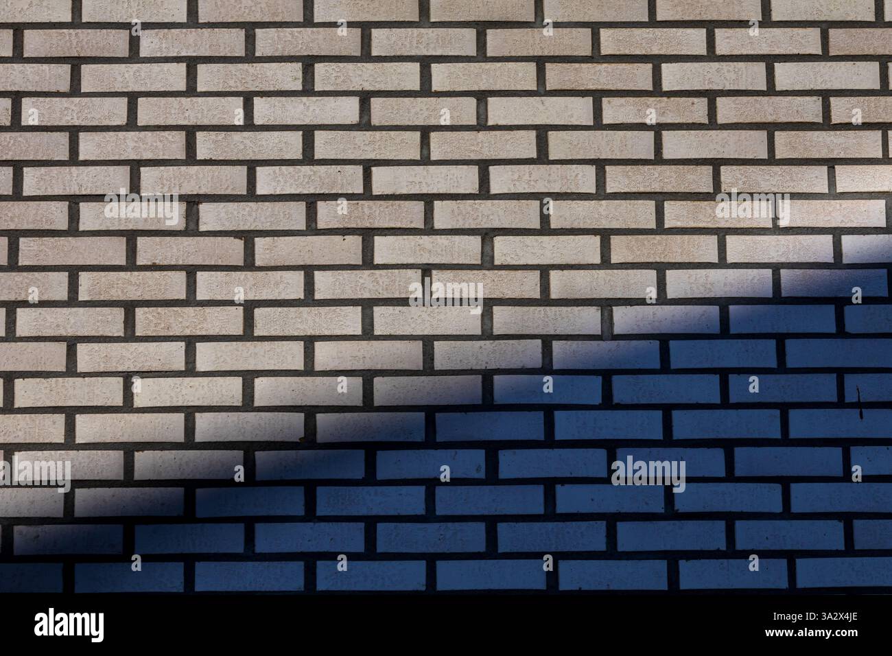 Un jeu d'ombres intéressant crée des formes triangulaires nettes sur un mur de briques, ajoutant de la profondeur et un contraste géométrique à la surface texturée. Banque D'Images