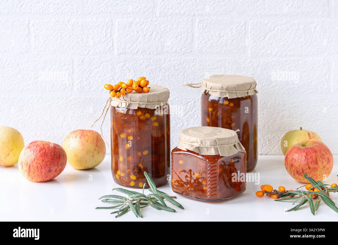 Une photographie magnifiquement stylisée de trois bocaux en verre avec argousier maison et confiture de pommes. Les bocaux sont recouverts de couvercles en papier et attachés avec des jumeaux Banque D'Images