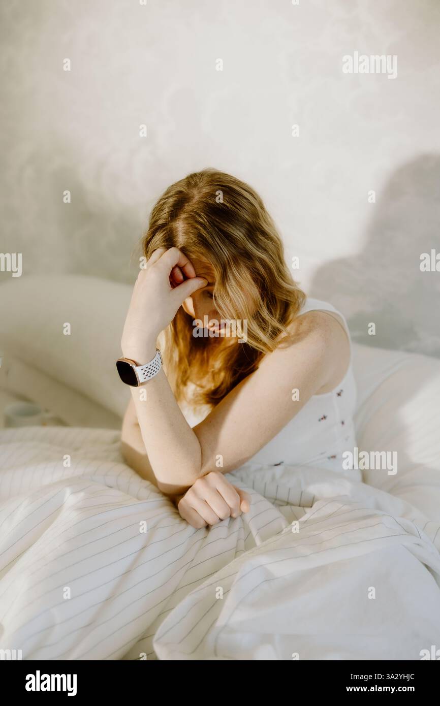 Une femme fatiguée est assise au lit, tenant sa tête dans un moment de stress Banque D'Images