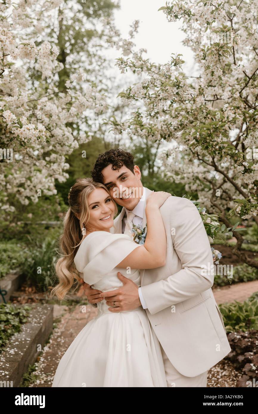 Mariée et mariée embrassent joyeusement sous les arbres en fleurs dans un jardin Banque D'Images