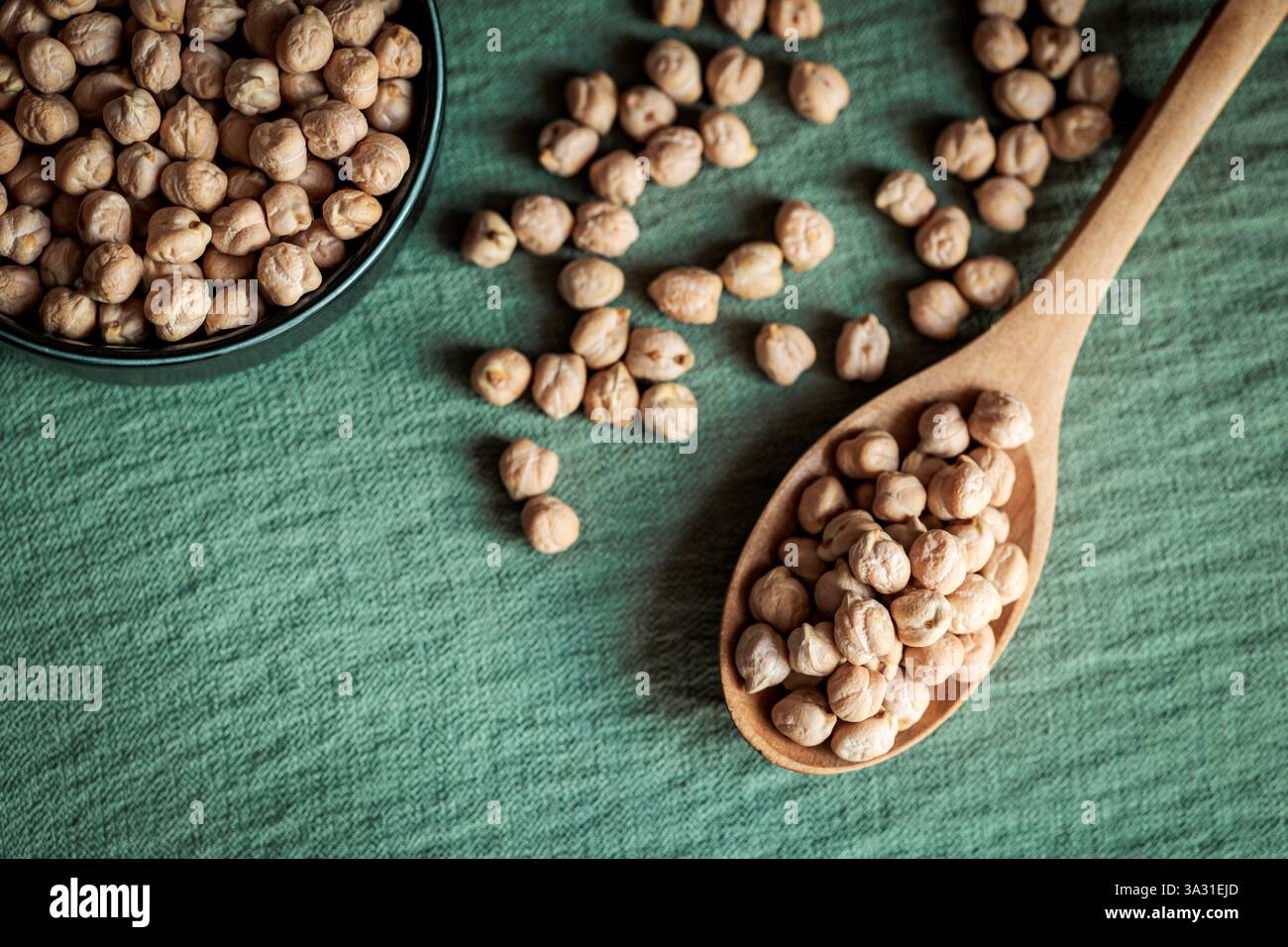 Vue de dessus de pois chiches séchés dans un bol en céramique et une cuillère en bois sur un fond vert, mettant en valeur des concepts alimentaires rustiques et sains Banque D'Images