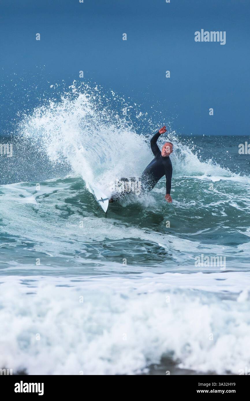 Un surfeur mâle mature qui fait une vague à Fistral, à Newquay, en Cornouailles, au Royaume-Uni. Banque D'Images