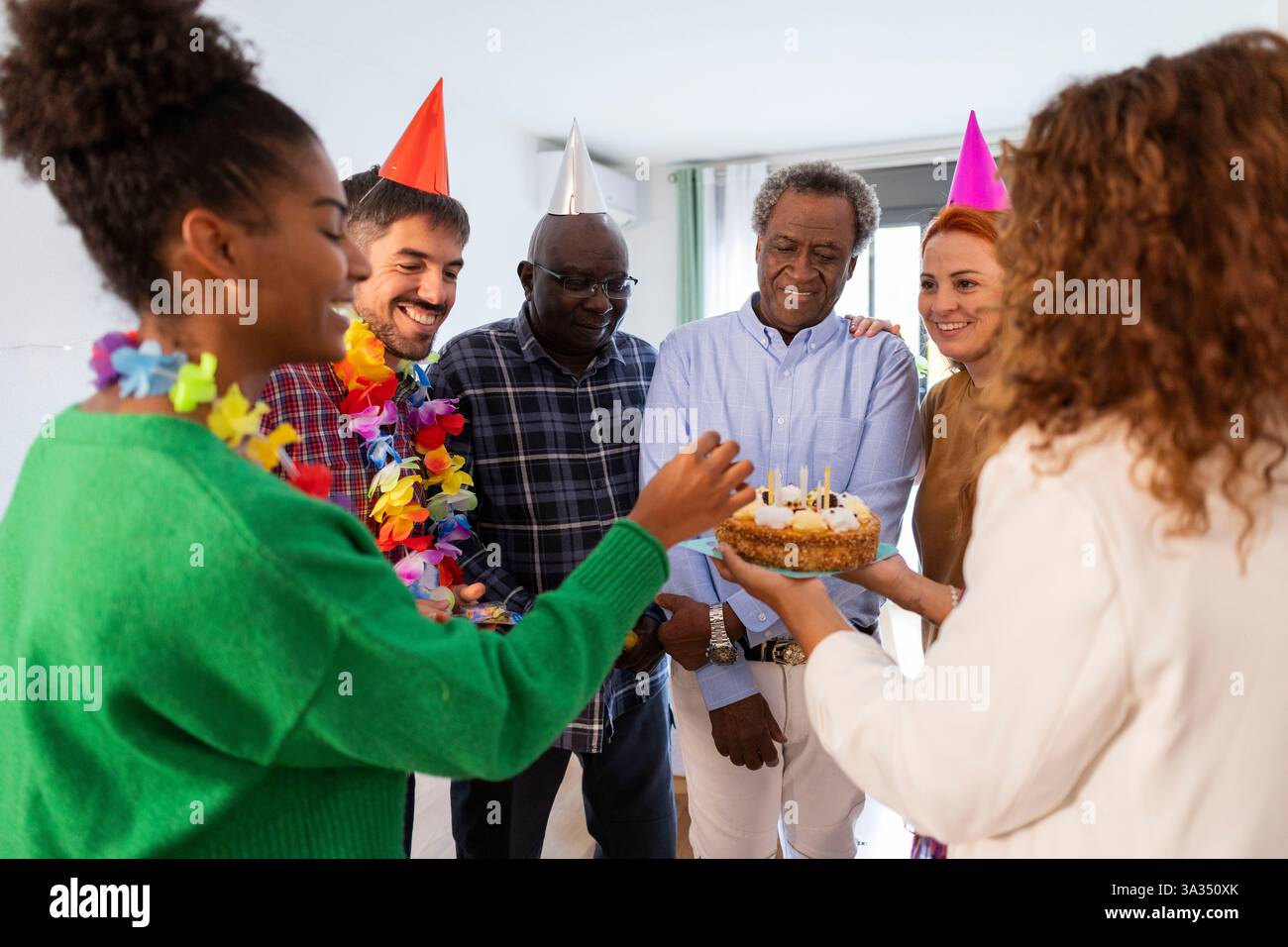 Un groupe animé de personnes célébrant un anniversaire avec des chapeaux de fête colorés et un gâteau. Ils partagent des sourires, créant une atmosphère chaleureuse et festive pleine de Banque D'Images