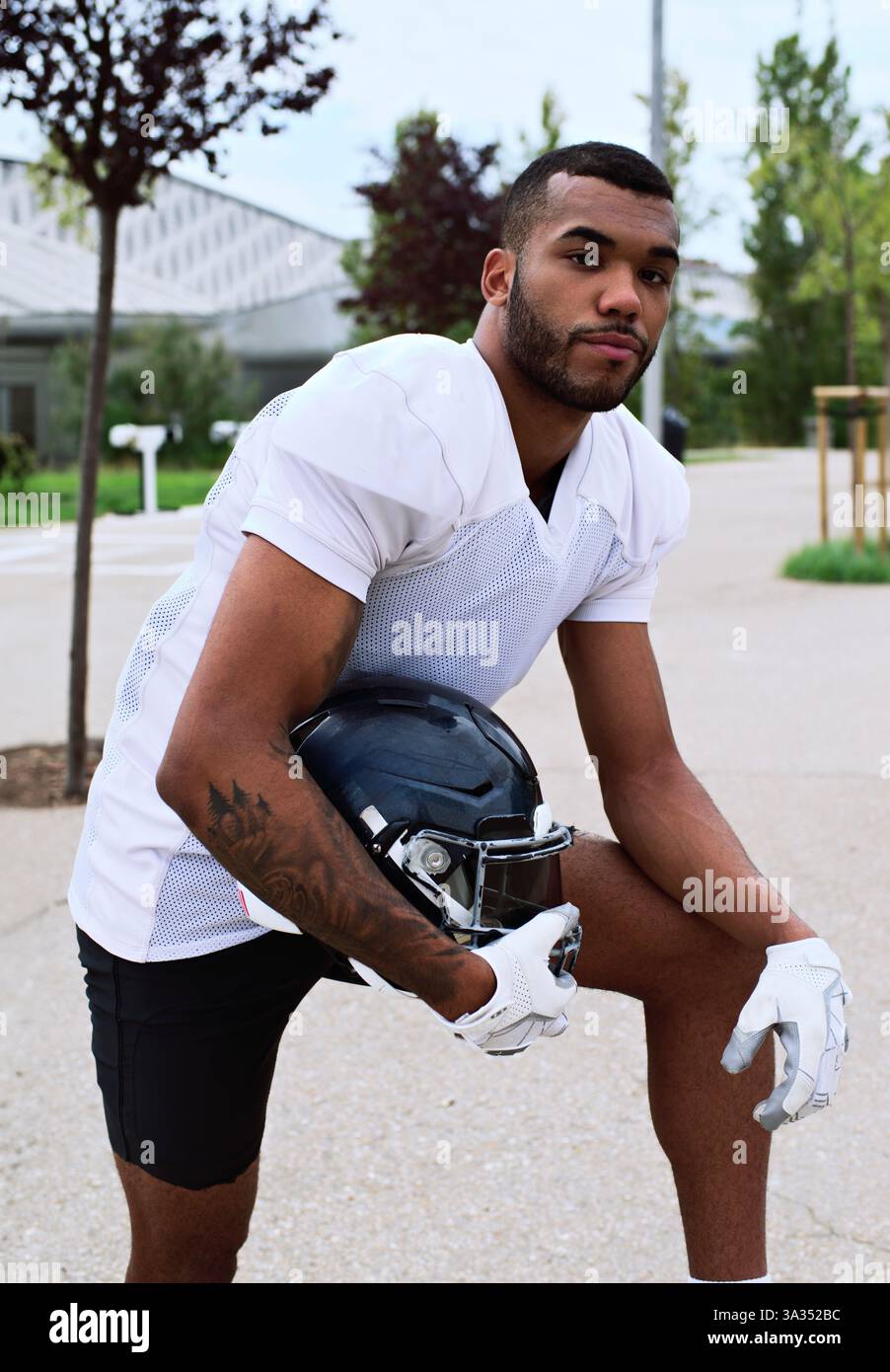 Un joueur de football américain confiant portant un maillot blanc tient un casque à l'extérieur. La scène incarne l'athlétisme, la détermination et l'esprit d'Ameri Banque D'Images