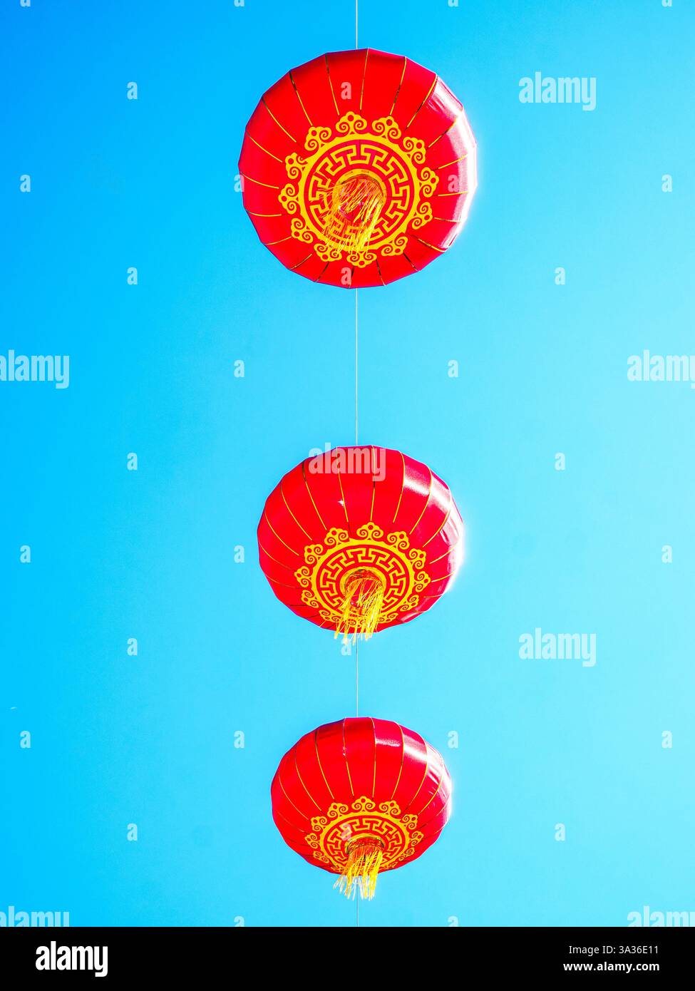 Trois lanternes rouges chinoises traditionnelles avec des détails dorés suspendus à un fil de fer contre un ciel bleu clair, symbolisant la chance et la prospérité. Banque D'Images