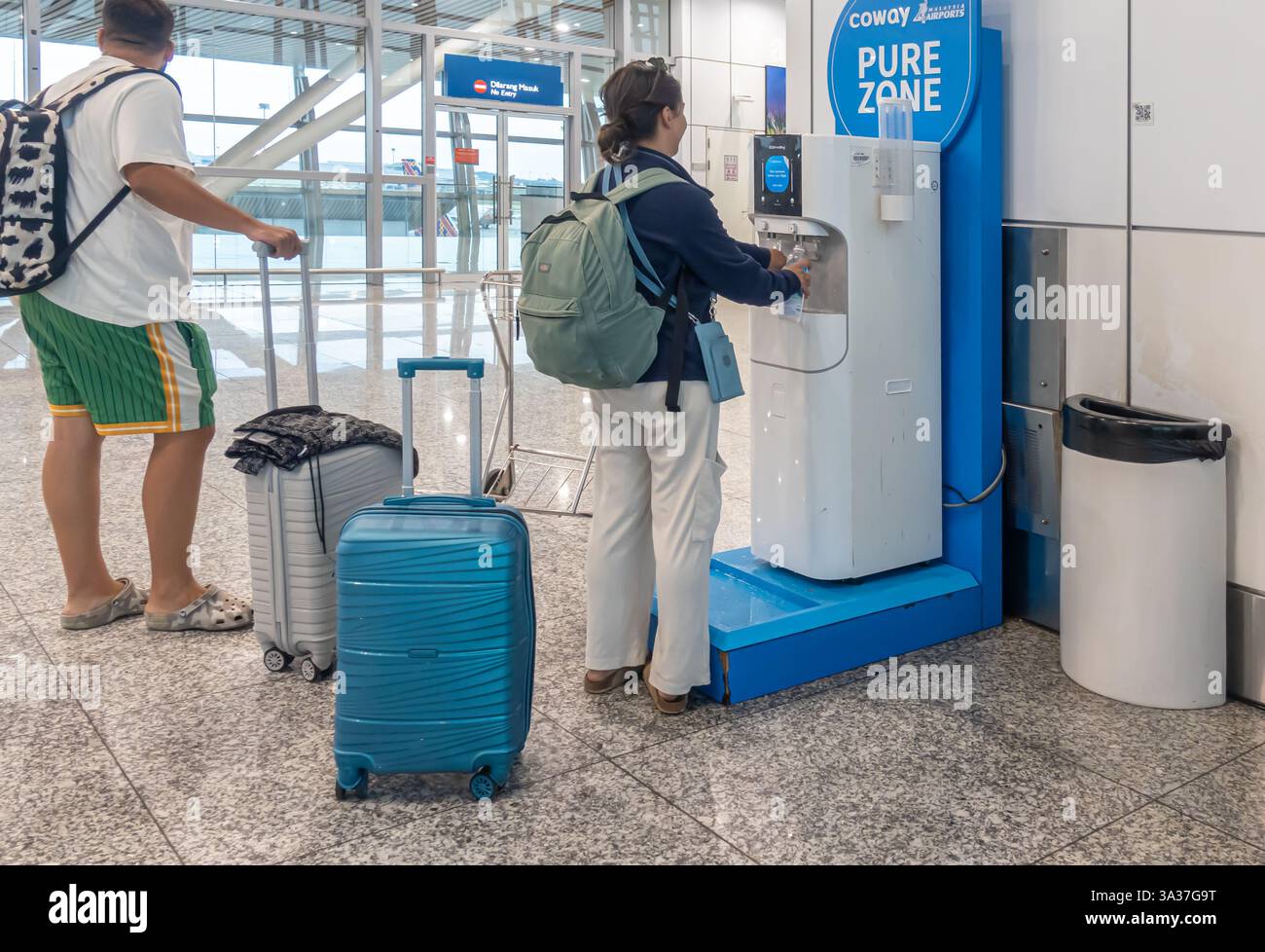 Un distributeur d'eau « PURE ZONE » à l'aéroport de Kuala Lumpur, avec personnes et bagages à proximité. Le distributeur d'eau, de marque Coway, est conçu pour le public Banque D'Images