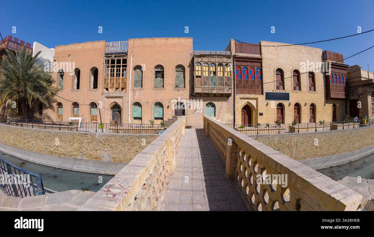 Un bâtiment historique en briques avec des fenêtres colorées et un palmier, vu d'un pont de pierre. En Irak, Bassorah Banque D'Images