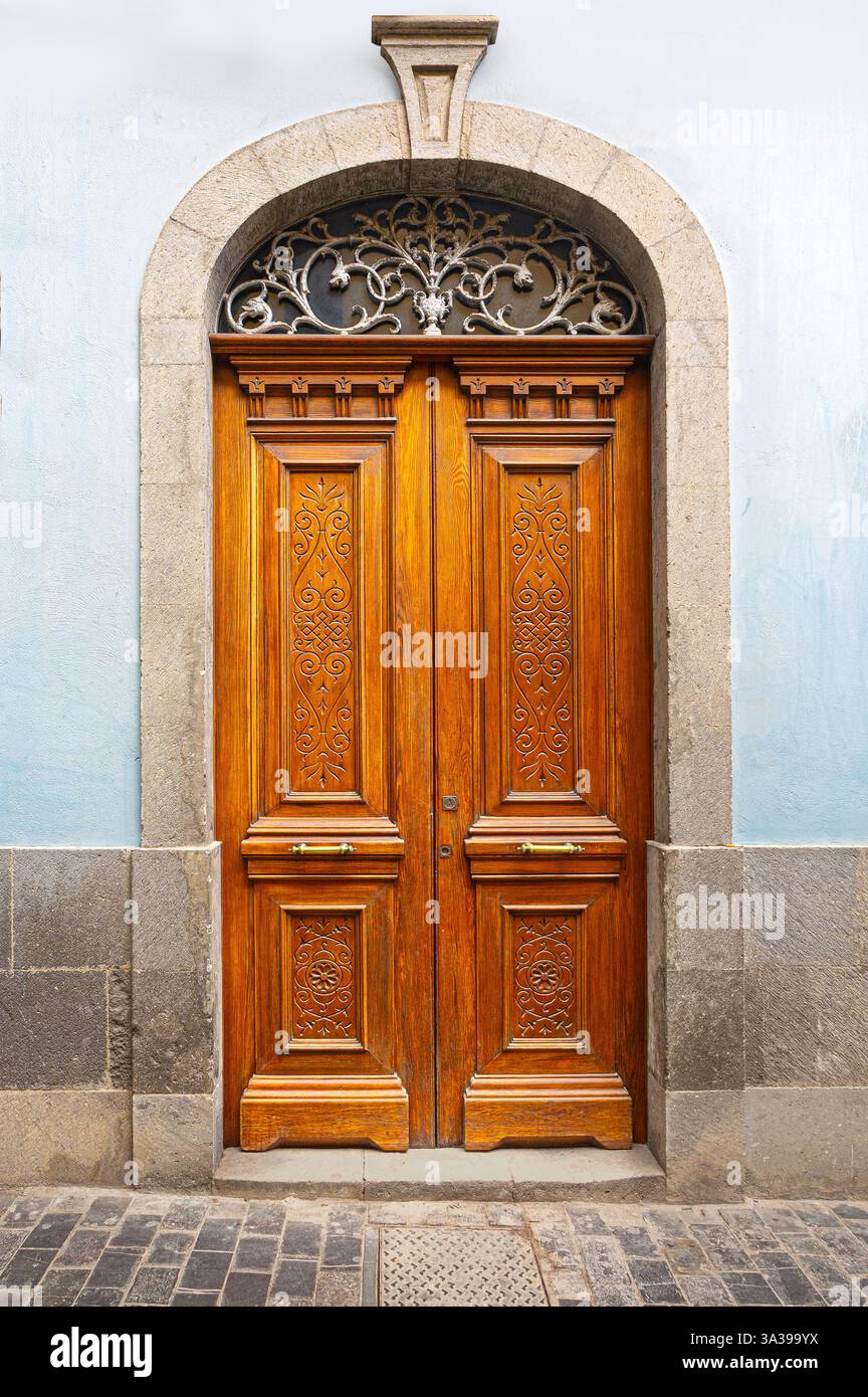 Double porte en bois ornée de sculptures complexes, d'un tableau arrière décoratif en ferronnerie et d'un cadre en pierre cintré, ajoutant une touche d'élégance à un buil Banque D'Images