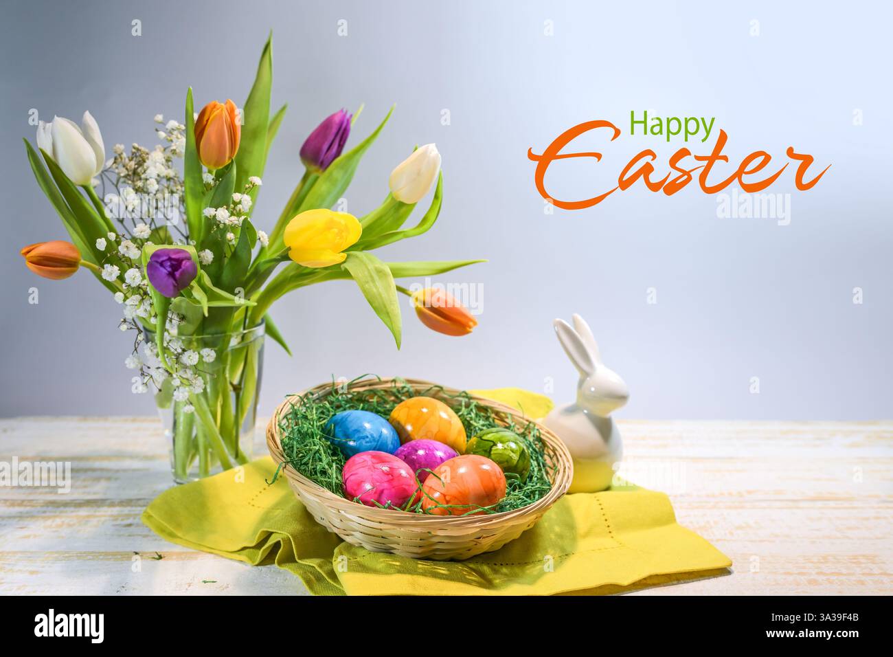 Oeufs de Pâques colorés dans un panier, bouquet de printemps avec des tulipes et un petit lapin, texte joyeuses Pâques, fond gris bleu clair, espace copie, sélectionné fo Banque D'Images