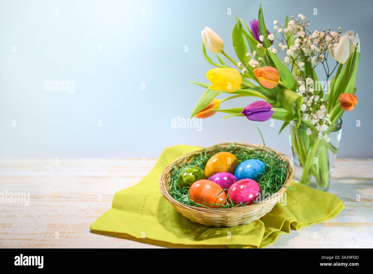 Oeufs de Pâques colorés dans un panier et un bouquet de printemps avec des tulipes sur bois clair sur un fond bleu, nourriture et décoration de vacances, espace copie, se Banque D'Images