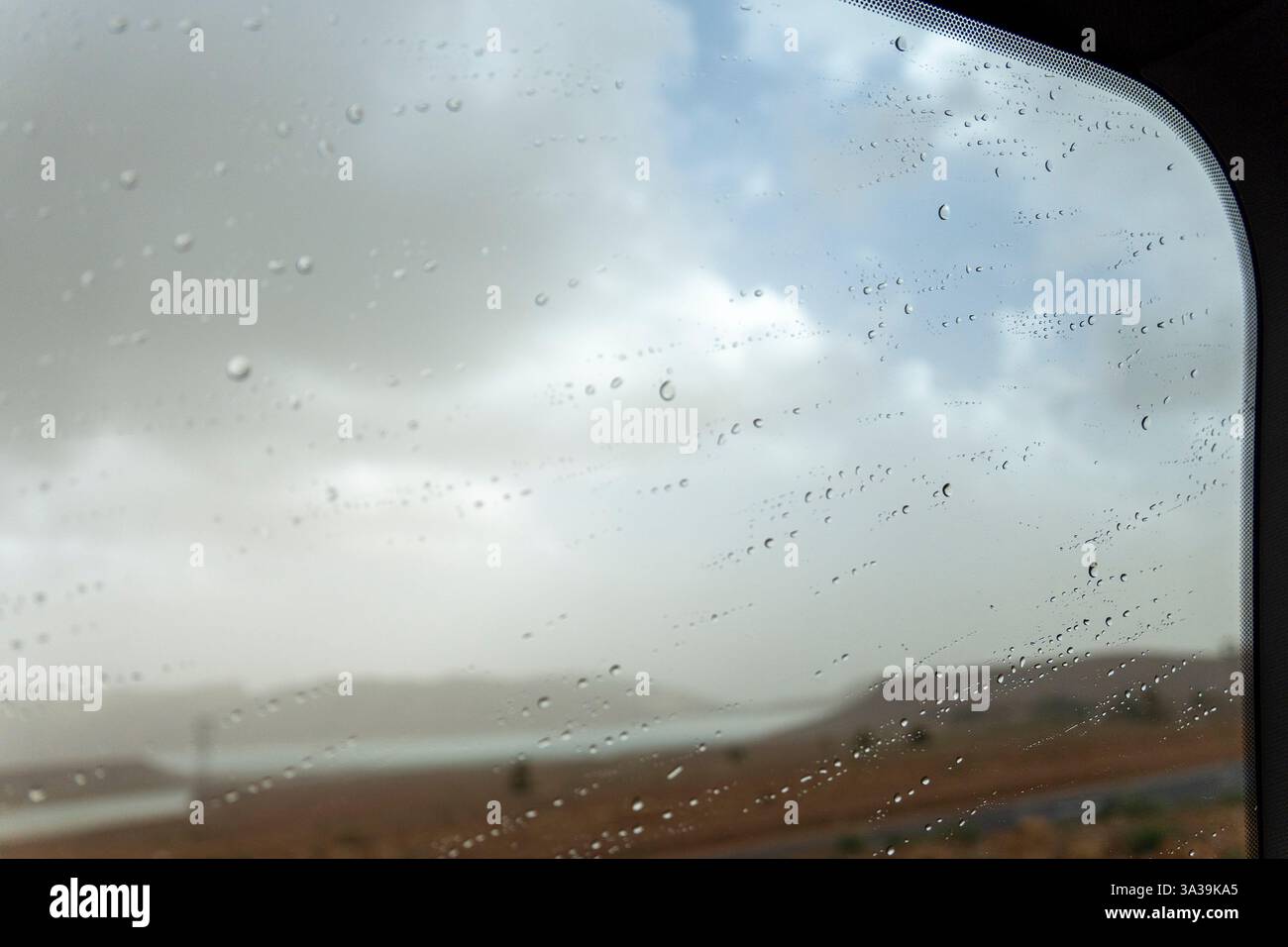 Une vue d'un ciel nuageux à travers une fenêtre couverte de gouttes de pluie Banque D'Images