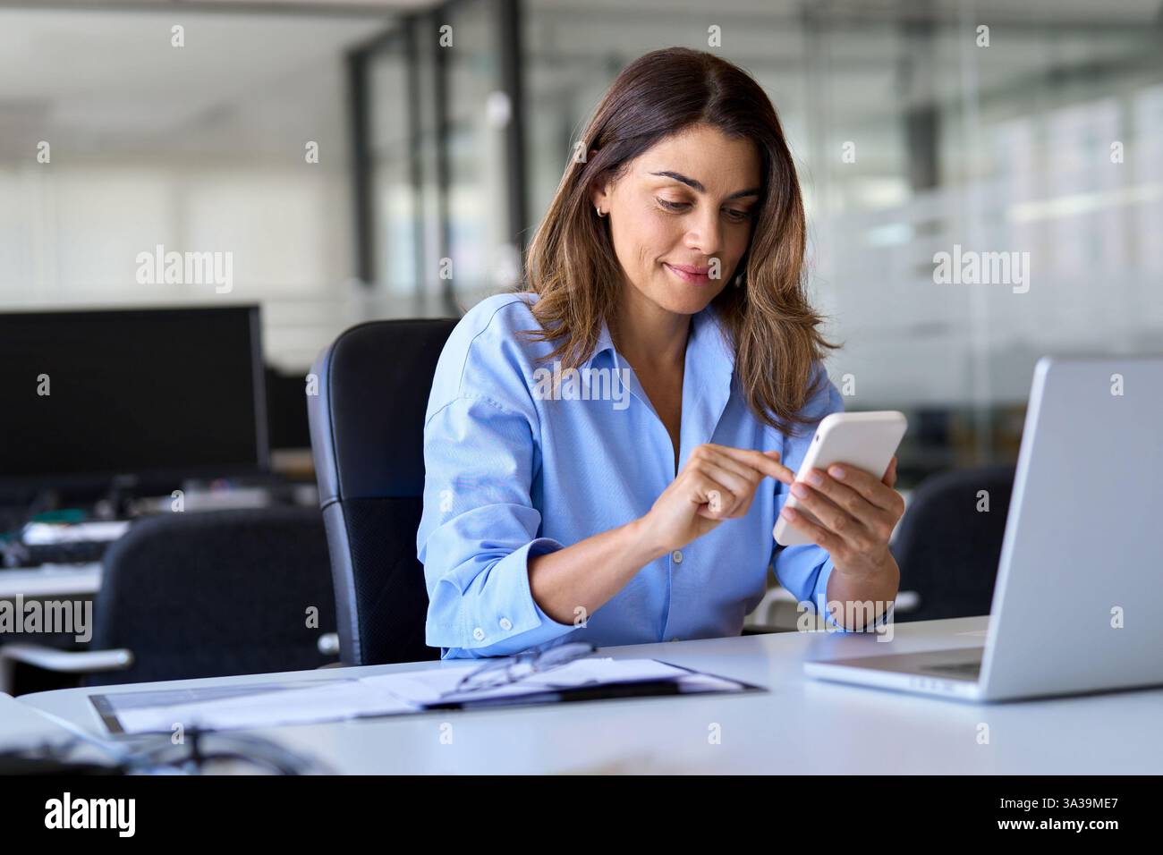 Heureux cadre de femme d'affaires mature utilisant le smartphone travaillant dans le bureau. Banque D'Images