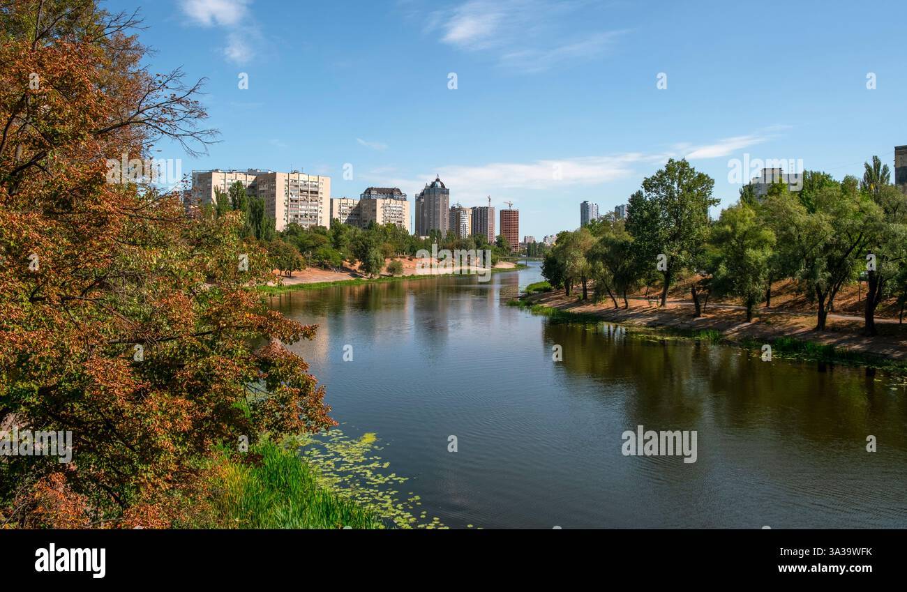 Une rivière tranquille reflète l'horizon tandis que les couleurs d'automne ornent le paysage, invitant des moments paisibles au cœur de la ville. Banque D'Images