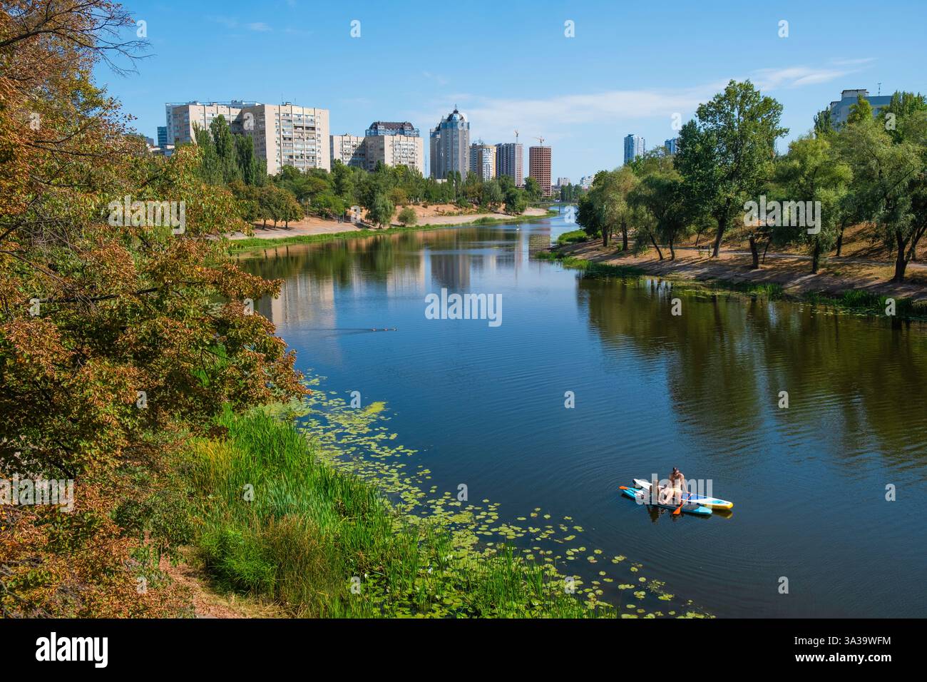 Kyib , Ukraine - 8 septembre 2023 : une journée paisible se déroule alors que les pagayeurs profitent des eaux douces, encadrées par une végétation luxuriante et des bâtiments imposants sous un ciel vibrant. Couple se reposant sur des planches de paddle à la rivière Dnipro Banque D'Images