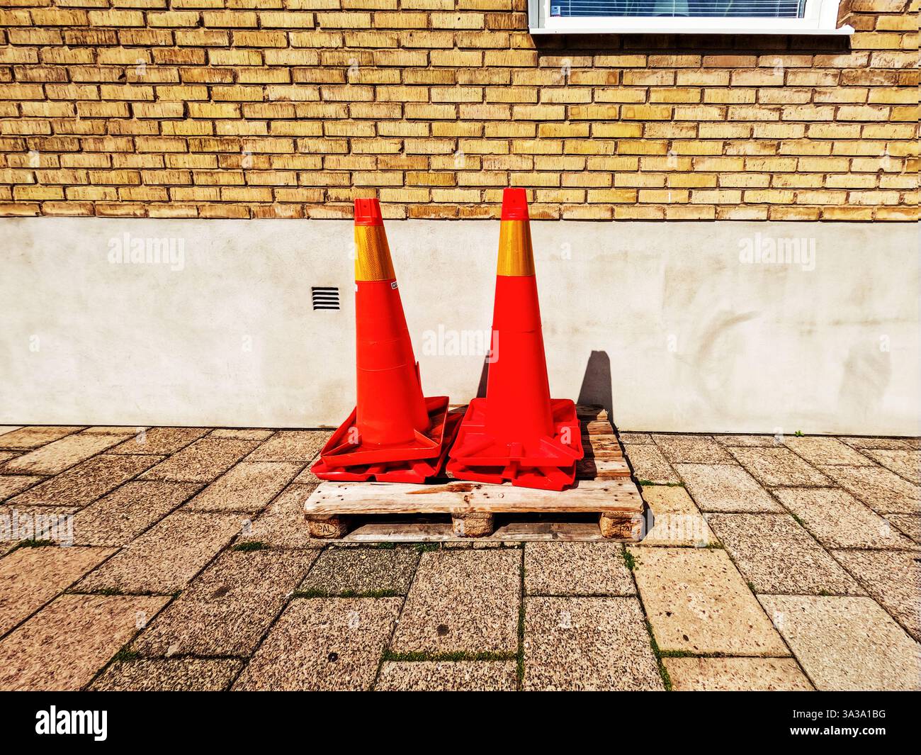 De grands cônes rouges se dressent sur une palette en bois devant une maison. Matériel de construction de routes. Cône pour marquer les routes pendant les réparations et clôturer o Banque D'Images