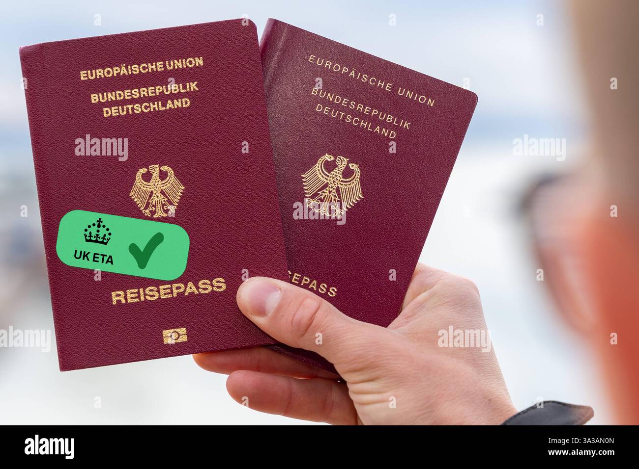 Bavière, Allemagne - 14 mars 2025 : PHOTOMONTAGE, une main tenant deux passeports allemands, l'autre portant un symbole vert de l'ETA britannique. L'autorisation de voyage numérique est nécessaire pour entrer au Royaume-Uni et est utilisée avec le passeport. *** FOTOMONTAGE, eine hand hält zwei deutsche Reisepässe, einer mit einem grünen UK ETA Symbol. Die digitale Reisegenehmigung ist für die Einreise nach Großbritannien erforderlich und wird mit dem Pass genutzt. Banque D'Images
