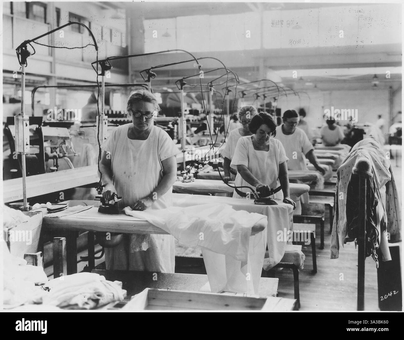 un environnement de travail de blanchisserie ou de textile, possiblement à la fin du xixe ou au début du xxe siècle. Il présente des femmes âgées qui travaillent comme blanchisserie, effectuant la tâche intensive de repasser à la main des vêtements ou du linge, une profession courante pour les femmes à l'époque. Banque D'Images