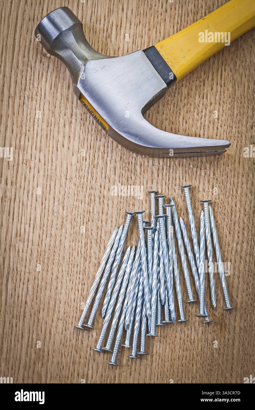 Pile de clous et marteau à griffes sur planche de bois Banque D'Images