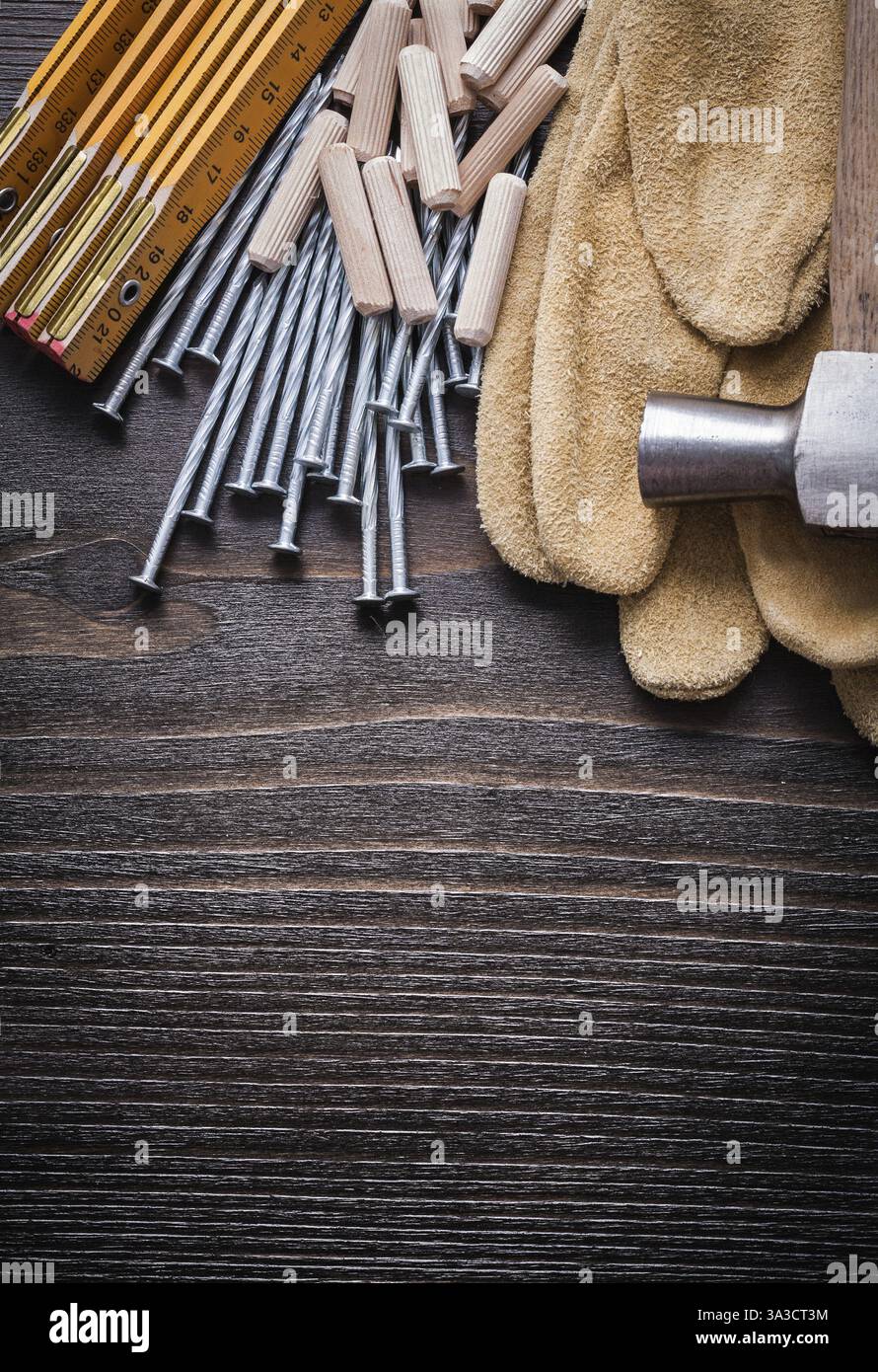 Mètre en bois tas de chevilles griffe marteau gants de protection bruns et clous en métal sur le concept de construction de vue de dessus de planche de bois vintage Banque D'Images