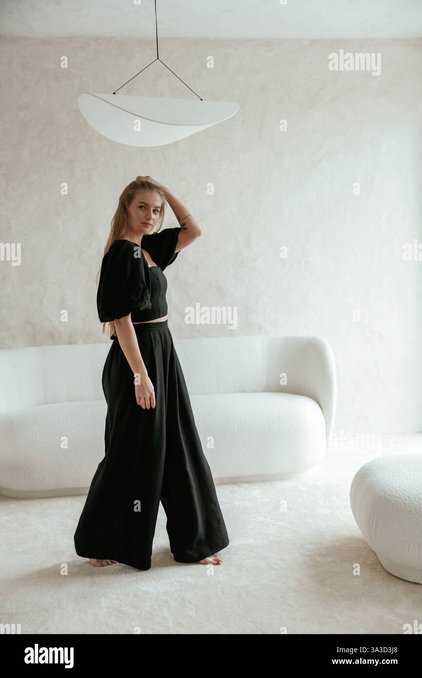 Belle jeune femme en robe noire est à l'intérieur, posant. Banque D'Images