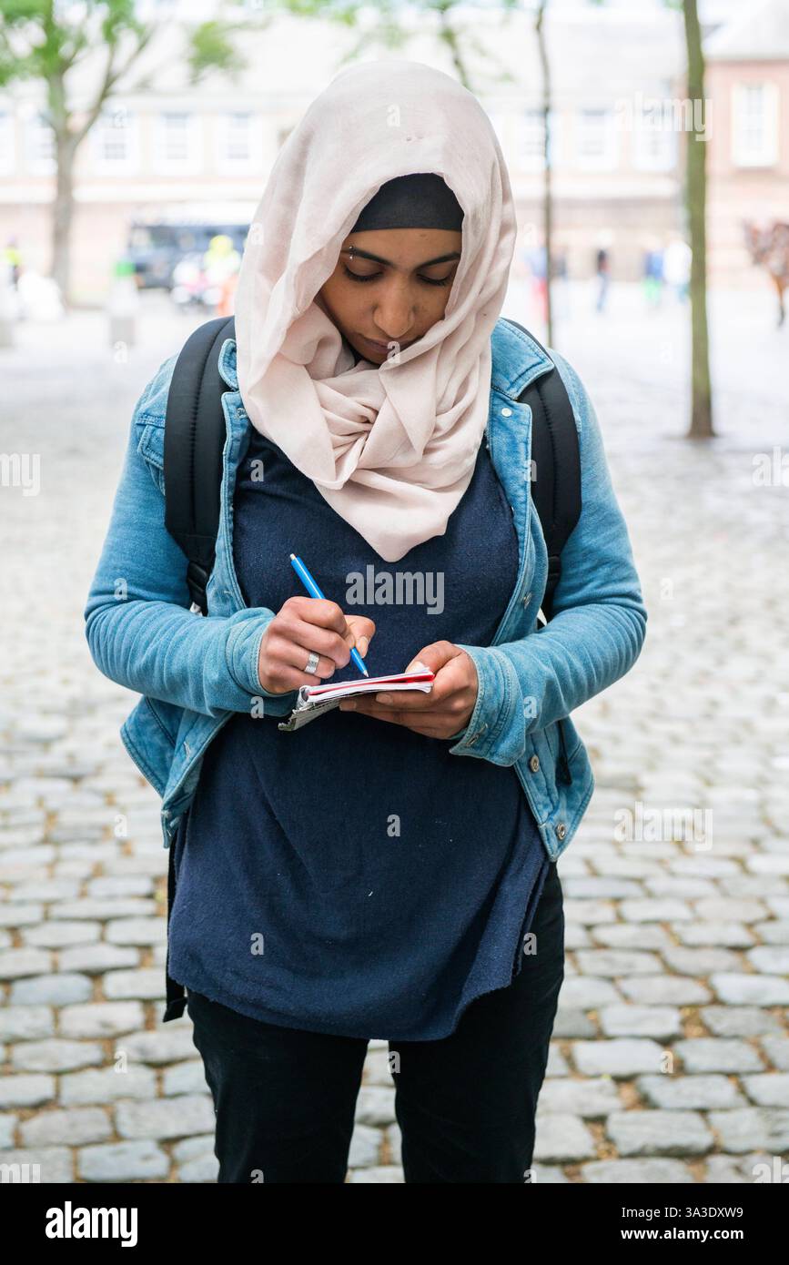 Jeune femme néerlando-égyptienne prenant des notes jeune femme néerlando-égyptienne prenant des notes, après avoir été confrontée à des partisans de Pegida. Breda, pays-Bas. Breda Binnenstad / Kasteelplein e.o. Noord-Brabant Nederland Copyright : xGuidoxKoppesxPhotox Banque D'Images