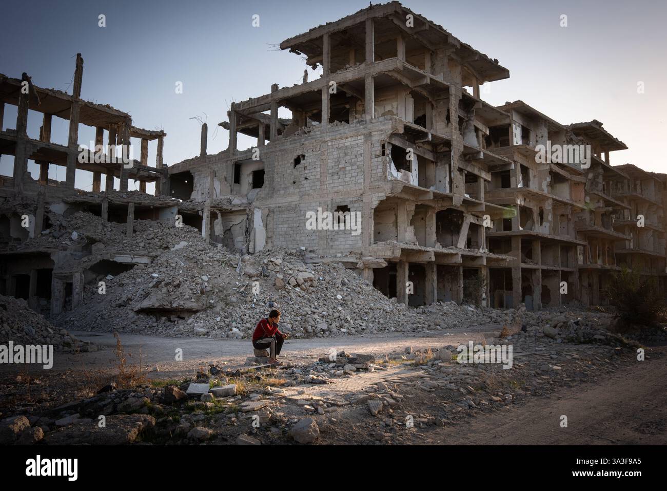 Yarmouk, Syrie. 14 mars 2025. Un jeune homme est assis devant un bâtiment en ruine. Yarmouk était le plus grand camp de réfugiés palestiniens en Syrie. Avant la guerre, environ un million de personnes y vivaient. Aujourd'hui, il ne reste plus que des gravats et des squelettes de bâtiments. Pendant la guerre syrienne, les forces anti-régime se sont installées à Yarmouk, transformant le camp en une ligne de front pour des batailles féroces. Après la chute du régime de Bachar Al-Assad, des dizaines de personnes ont décidé de revenir, certaines pour essayer de réparer les ruines de leurs maisons, d'autres simplement pour les voir une dernière fois. Crédit : SOPA images Limited/Alamy Live News Banque D'Images