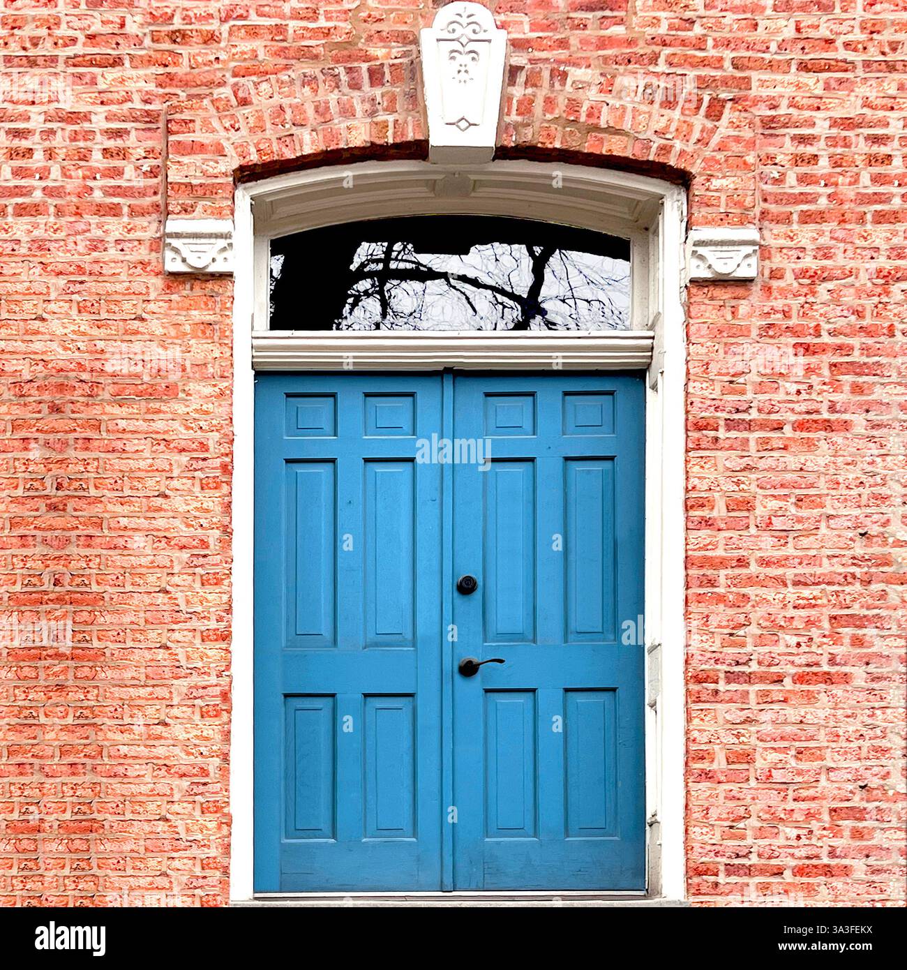 Portes doubles bleues situées dans une façade historique en briques roses, encadrées par des détails en pierre blanche ornés et une élégante fenêtre cintrée. Banque D'Images