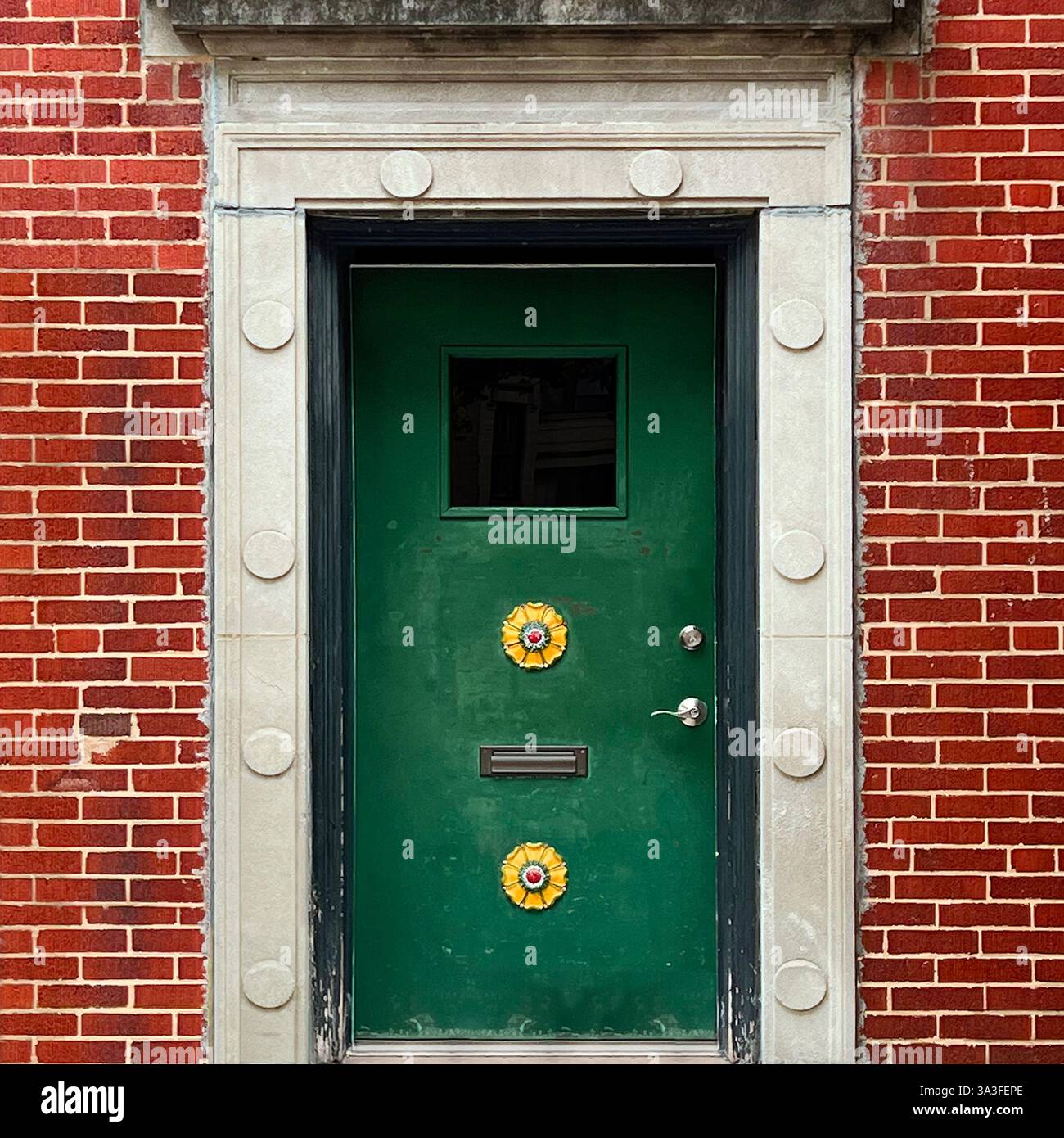 Porte verte avec des ornements floraux jaunes uniques dans une façade historique en briques rouges, encadrée par une bordure en pierre décorative avec des accents circulaires. Banque D'Images