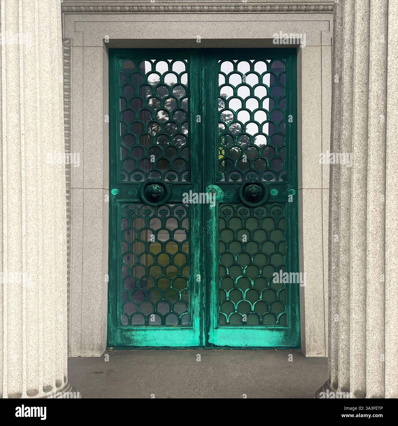 Portes en fer forgé vert patiné avec motif écailles de poisson, heurtoirs de porte à tête de lion au grand mausolée en pierre encadré par des colonnes classiques. Banque D'Images