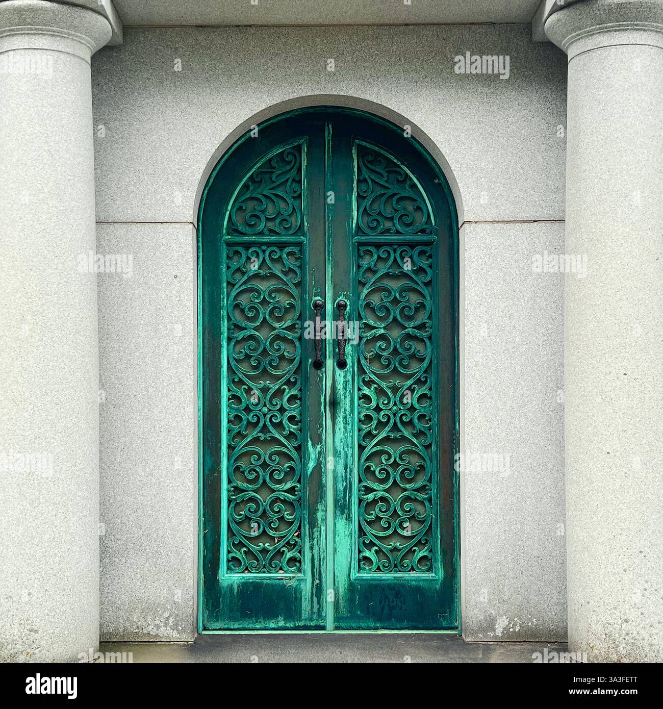 Élégantes portes en fer forgé vert patiné avec des volutes complexes, encadrées par des colonnes de pierre lisses dans une entrée de tombeau historique. - Image de stock capturée avec un smartphone
