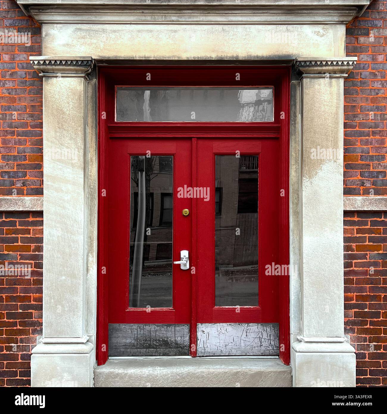 Élégantes portes doubles rouges avec panneaux de verre dans une façade historique en calcaire, encadrée par des colonnes. Banque D'Images