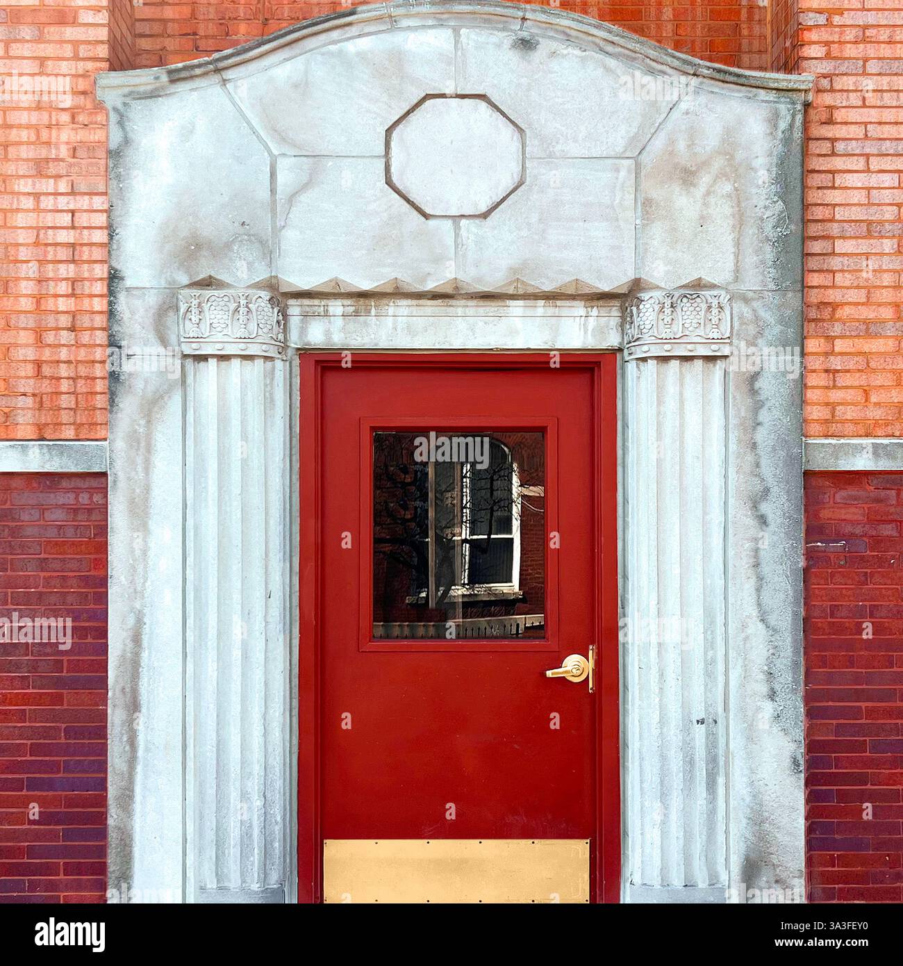 Porte rouge dans une grande entrée en pierre, soulignée par des colonnes cannelées symétriques et un octogone géométrique proéminent. Banque D'Images