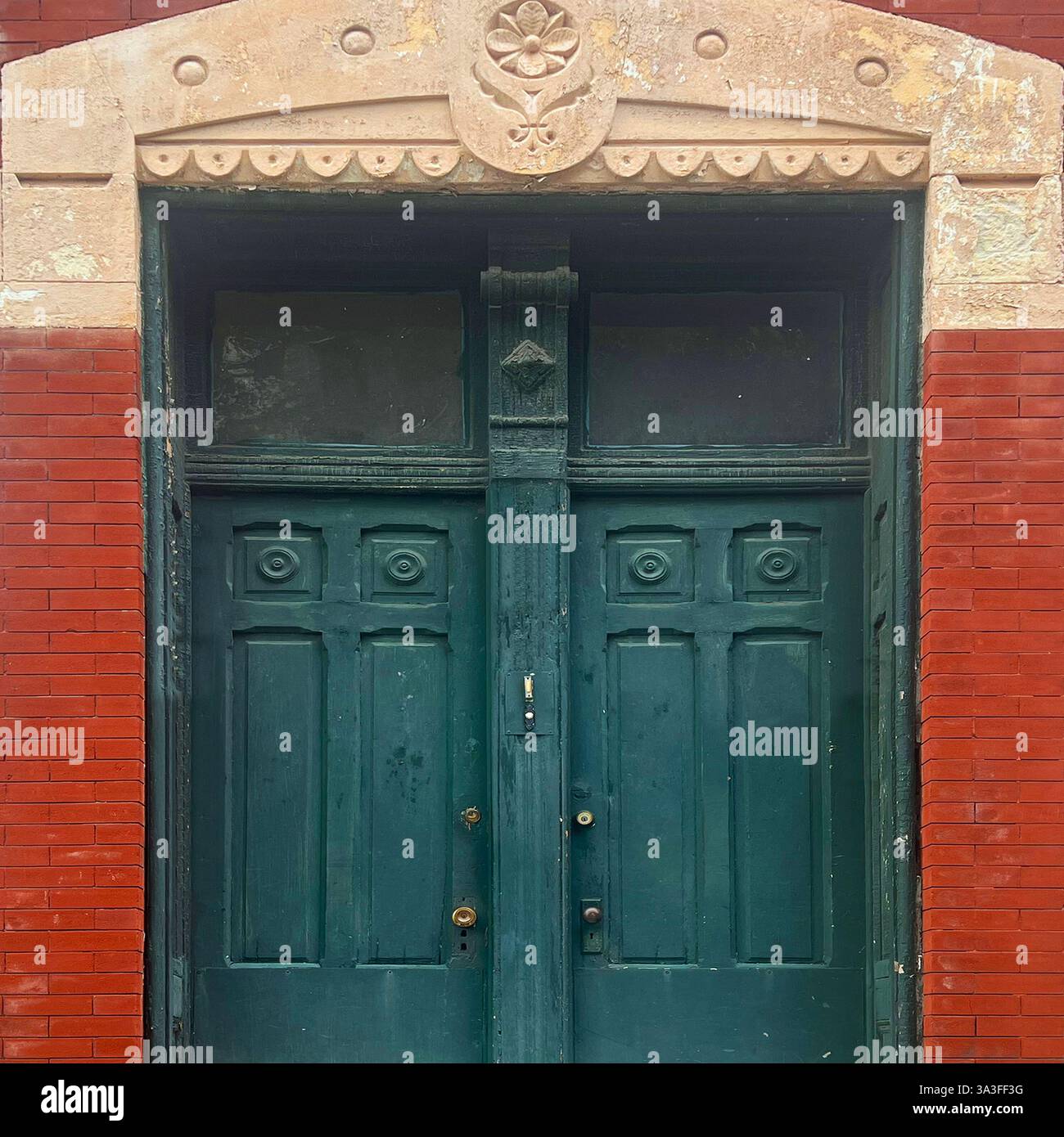 Portes doubles vertes vieillies avec des détails sculptés complexes et une arche décorative en pierre, placées contre une façade en briques rouges d'un bâtiment historique. Banque D'Images