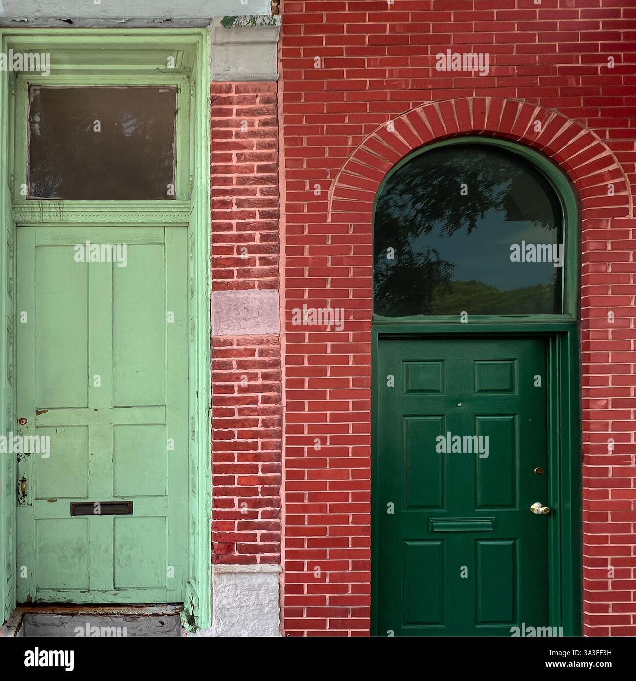 Deux portes vertes contrastées serties en brique rouge, l'une vieillie et altérée tandis que l'autre plus récente et raffinée, mettant en valeur la diversité architecturale. Banque D'Images