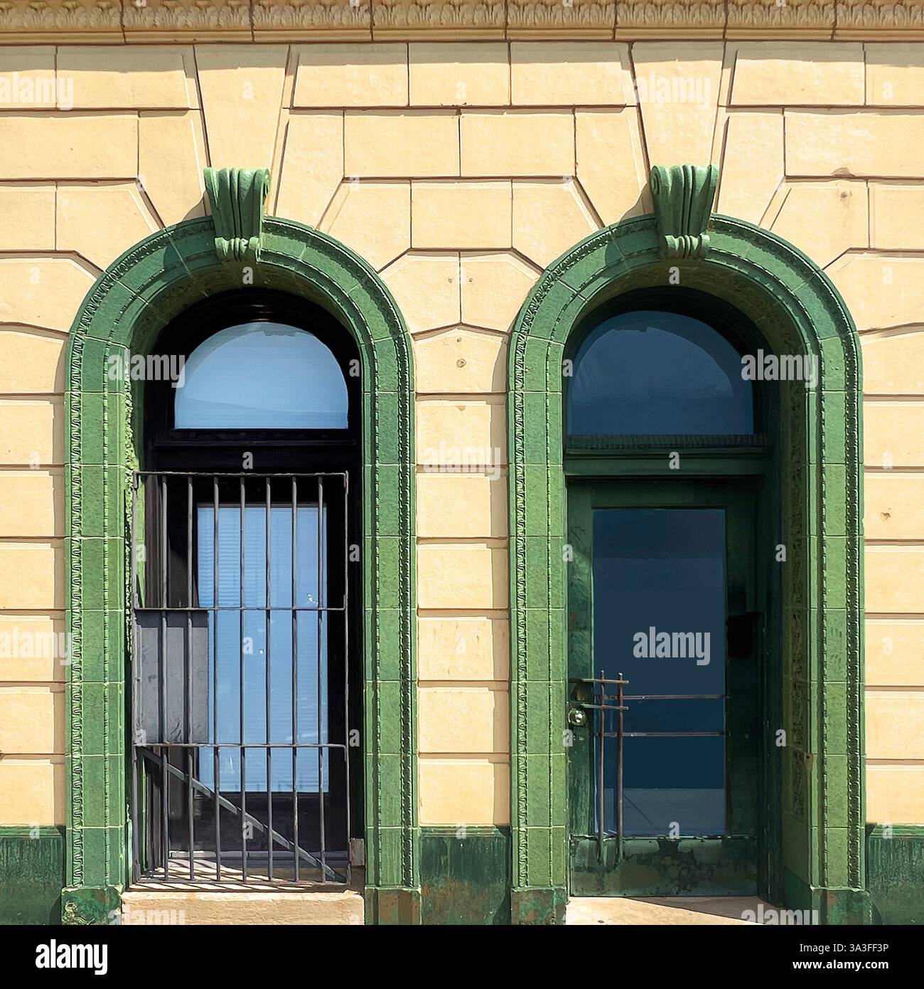 Porte et fenêtre historiques arquées encadrées de pierres vertes ornées de détails ornés, arborant des barres de sécurité en métal, placées contre une façade en pierre jaune. Banque D'Images