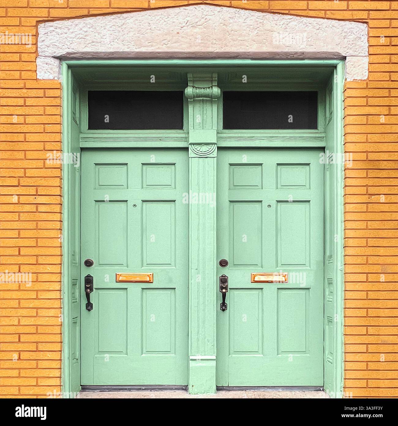 Élégantes portes doubles vert menthe avec moulures complexes, encadrées par une façade en briques jaunes chaudes et une arche décorative en calcaire. - Image de stock capturée avec un smartphone