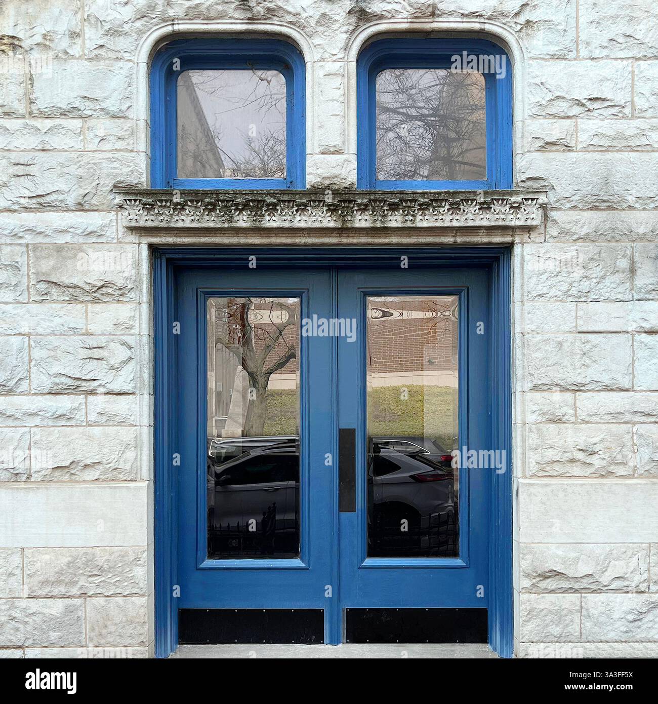 Élégantes portes doubles bleues avec doubles fenêtres cintrées, encadrées par une façade en pierre. - Image de stock capturée avec un smartphone