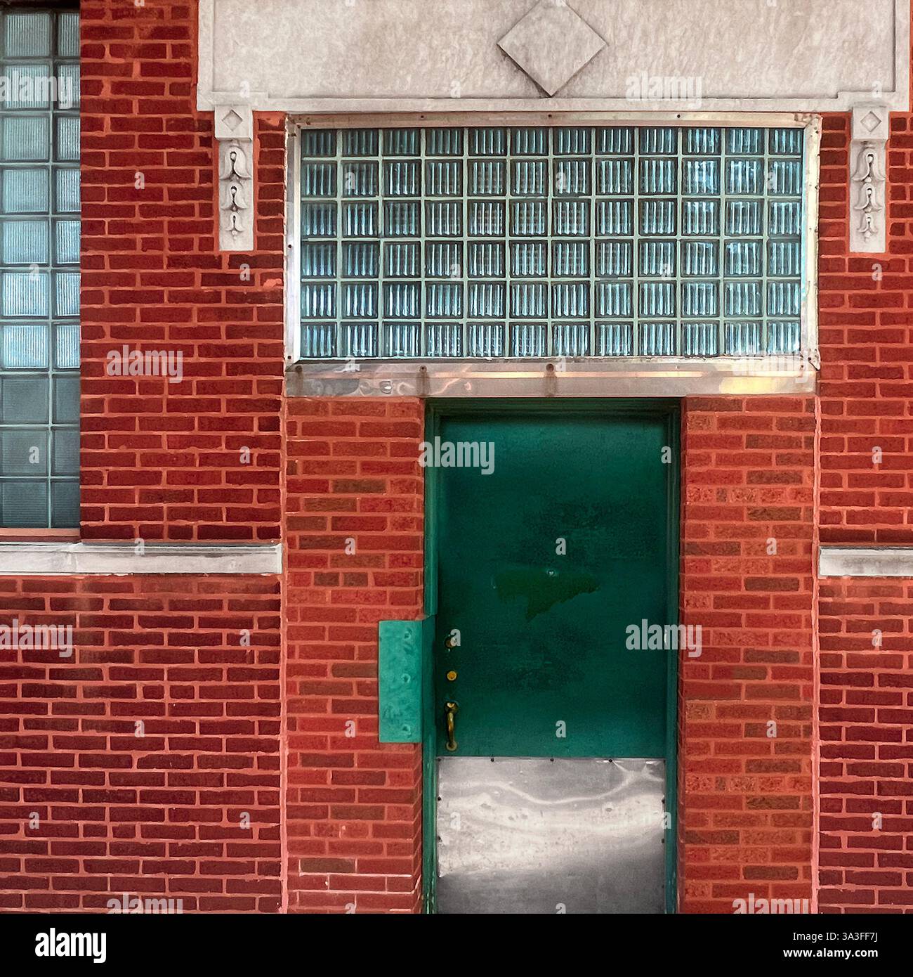 Porte en métal vert placée dans un bâtiment en briques rouges, encadrée par des blocs de verre industriels et des détails architecturaux décoratifs. - Image de stock capturée avec un smartphone