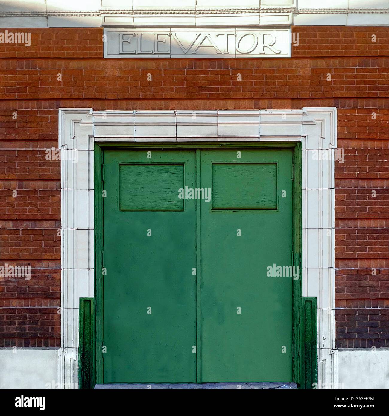 Portes d'ascenseur vertes vintage situées dans une façade en briques rouges et en pierre blanche, avec un panneau gravé « ASCENSEUR ». Banque D'Images