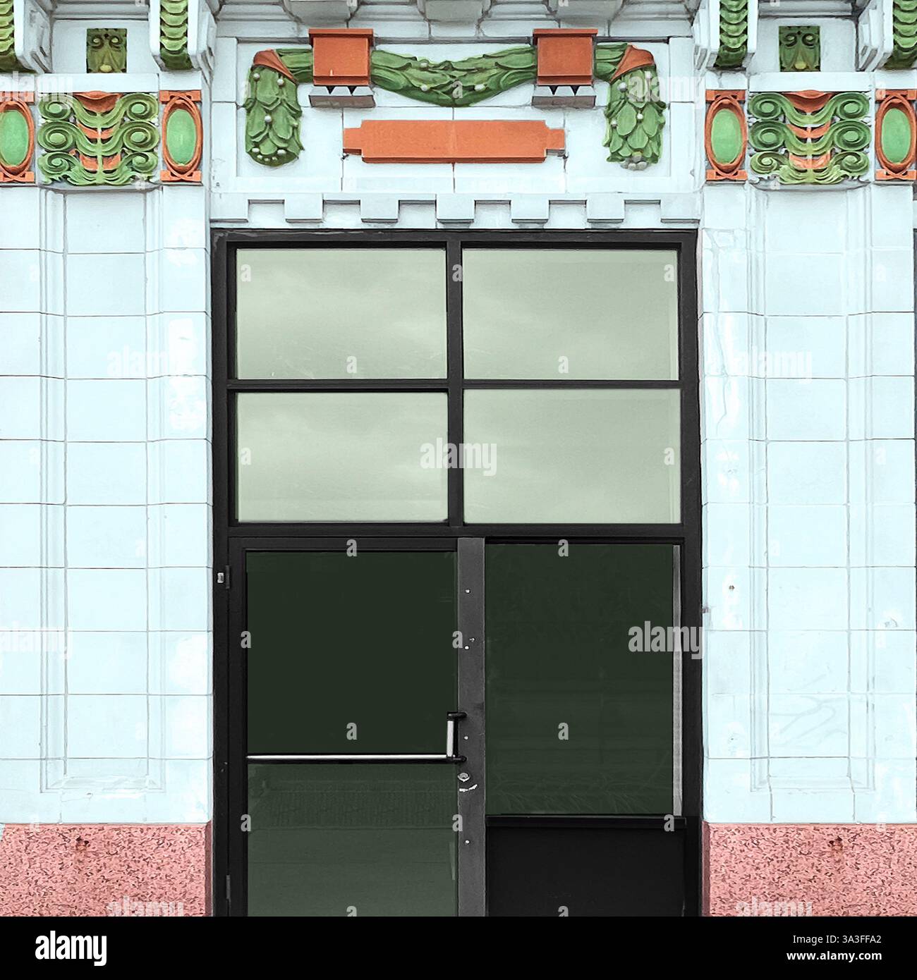 Entrée art déco ornée d'une porte vitrée dans une façade en terre cuite vitrée blanche, ornée de décorations vertes et oranges, dont des guirlandes. Banque D'Images