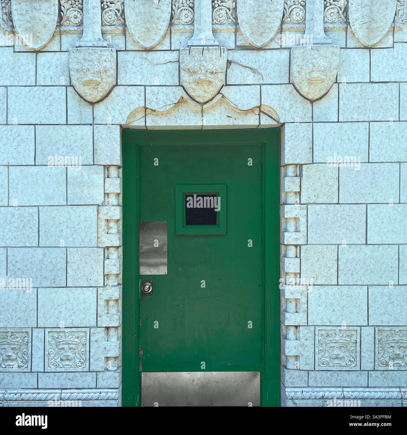 Porte en métal vert avec une petite fenêtre carrée, située dans une façade en pierre blanche ornée de visages sculptés à Chicago. - Image de stock capturée avec un smartphone