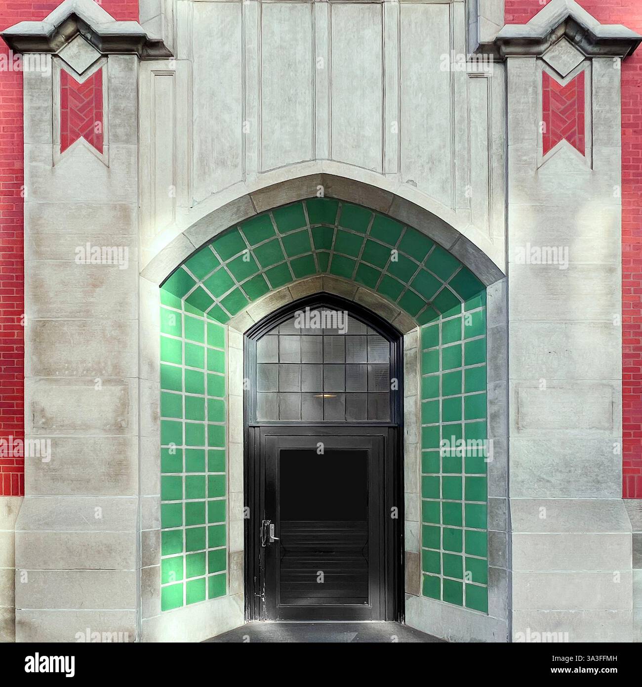 Entrée voûtée de style gothique, encadrée par des carreaux verts, des détails calcaires et des accents de briques rouges dans un bâtiment urbain historique. Banque D'Images