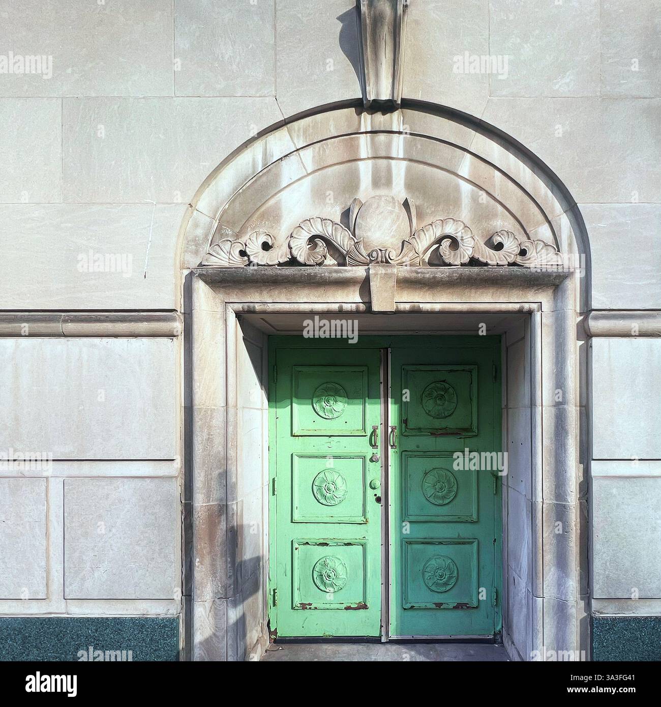Porte double vert menthe avec des sculptures florales complexes, encadrées par une arche en pierre ornée sur un bâtiment historique en pierre calcaire. Banque D'Images