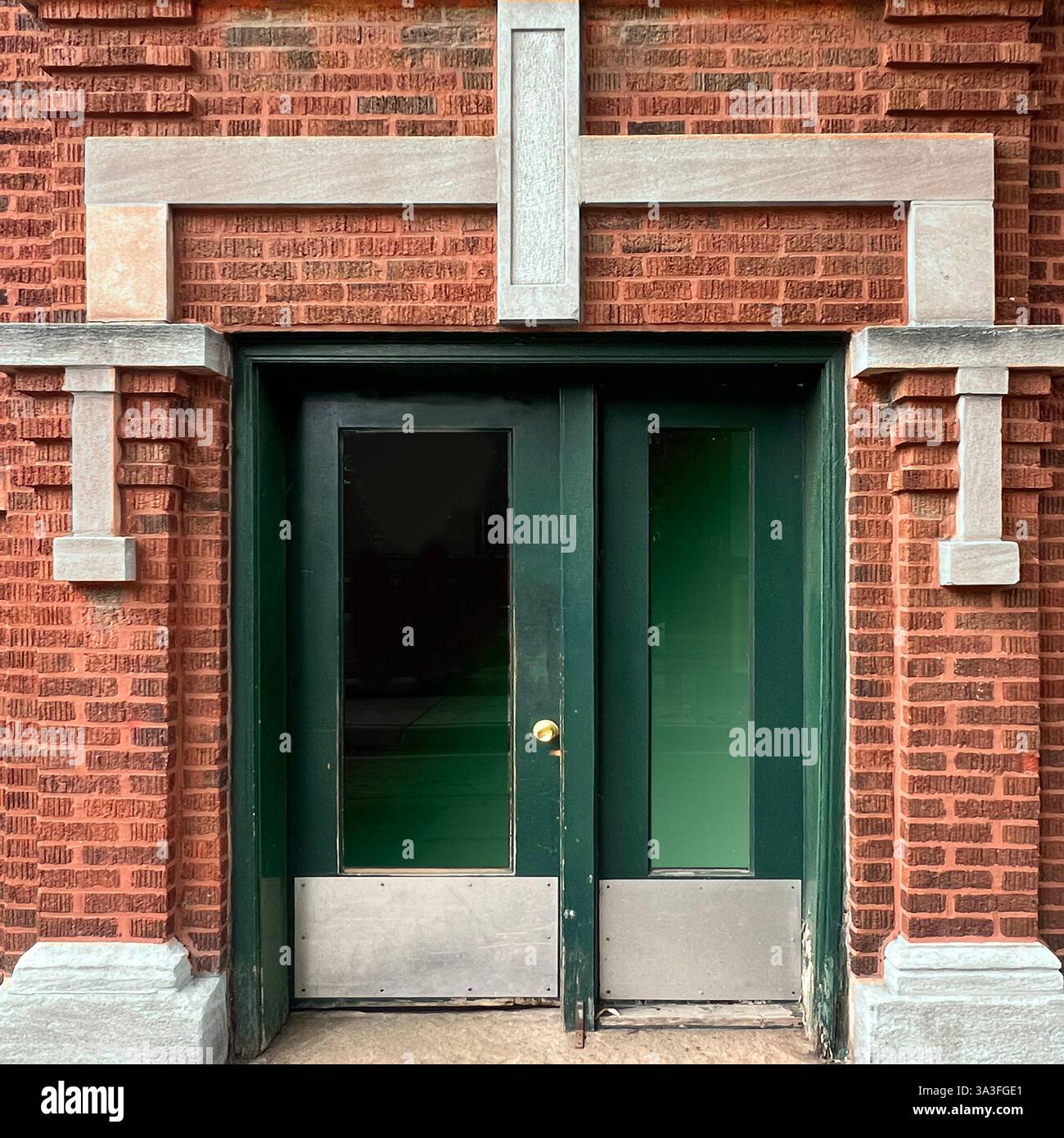 Double porte vert foncé avec panneaux de verre et plaques de pied en métal encadrées par la pierre décorative et la façade en briques brunes à Chicago. - Image de stock capturée avec un smartphone