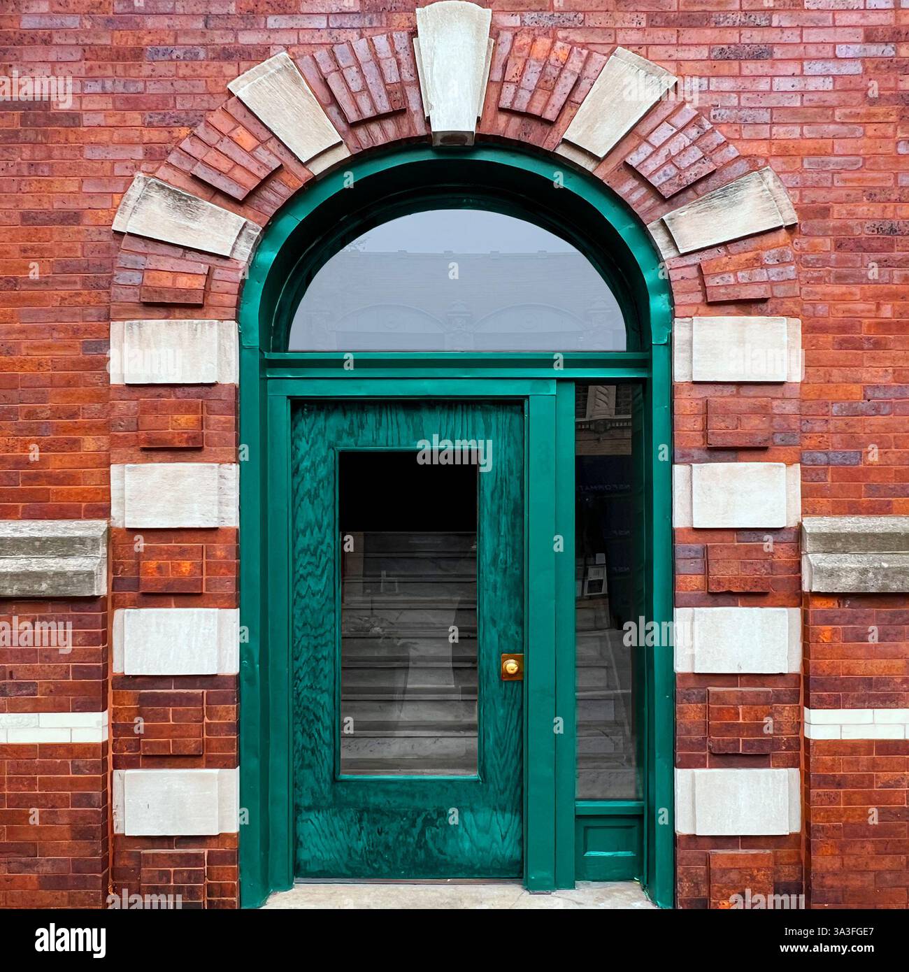 Entrée urbaine vintage avec un bois vert sarcelle avec un grand panneau de verre, encadré par une fenêtre voûtée et une brique alternée détaillée. Banque D'Images