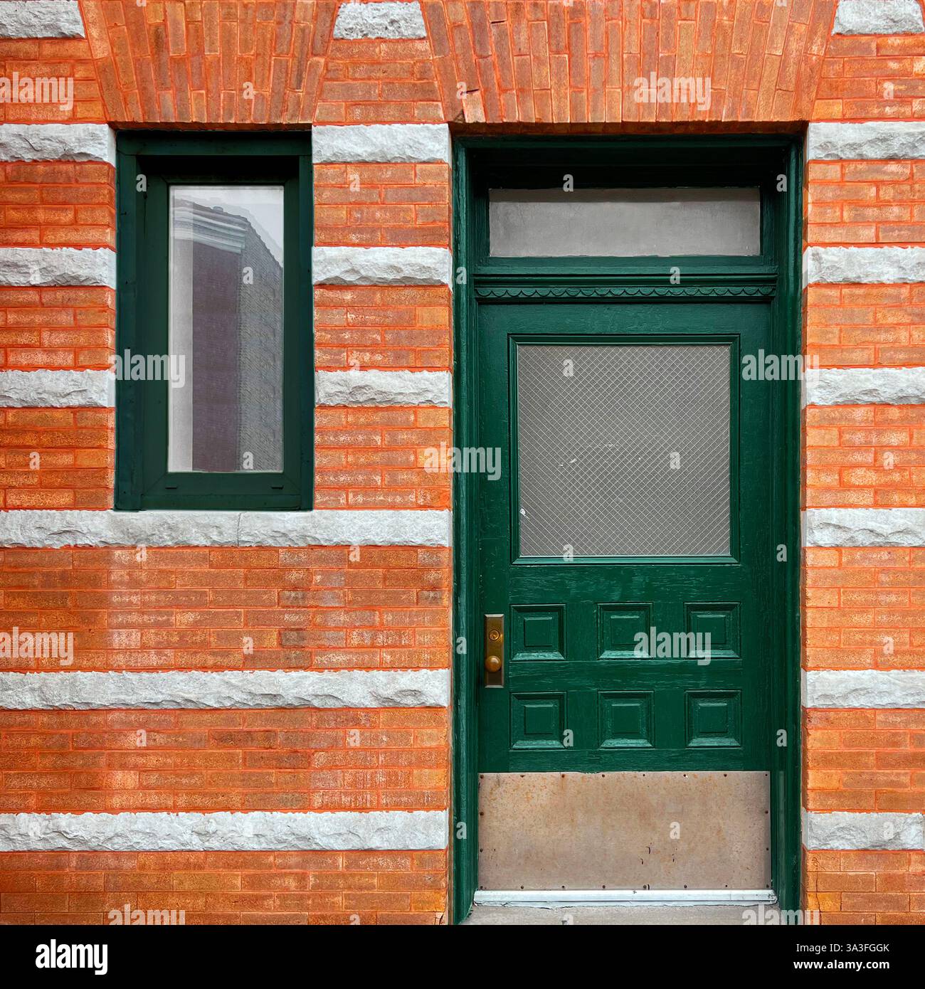 Porte en bois vert foncé avec panneau de verre texturé et quincaillerie en laiton dans une façade en pierre orange et blanche avec des bandes de pierre décoratives à Chicago. - Image de stock capturée avec un smartphone