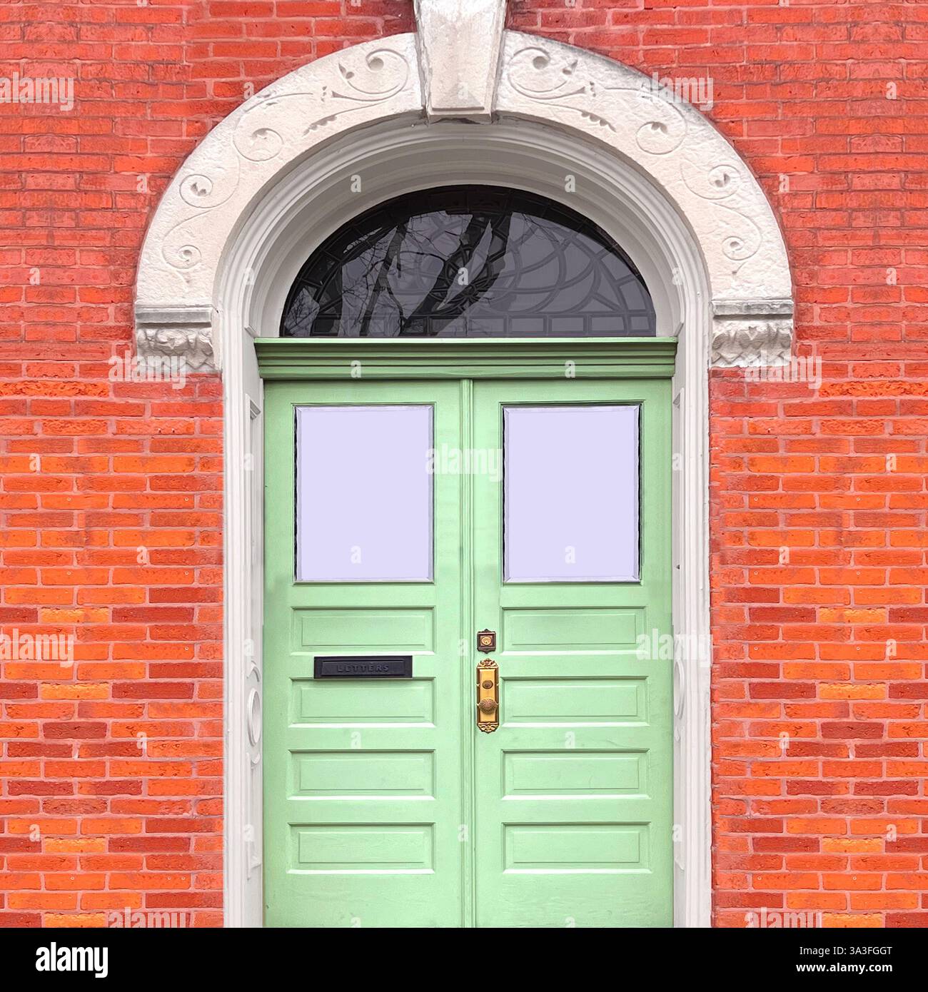 Porte double vert menthe avec quincaillerie en laiton et fenêtre de tableau arrière ornée arquée dans la façade en brique oranage avec pierres décoratives à Chicago. - Image de stock capturée avec un smartphone