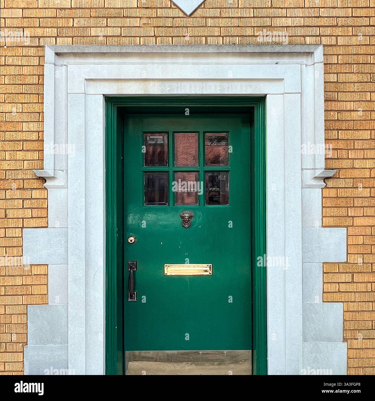Porte verte avec des panneaux de verre, un heurtoir décoratif de porte à tête de lion, et une fente de courrier en laiton, encadrée par une architrave de pierre blanche à l'intérieur - Image de stock capturée avec un smartphone